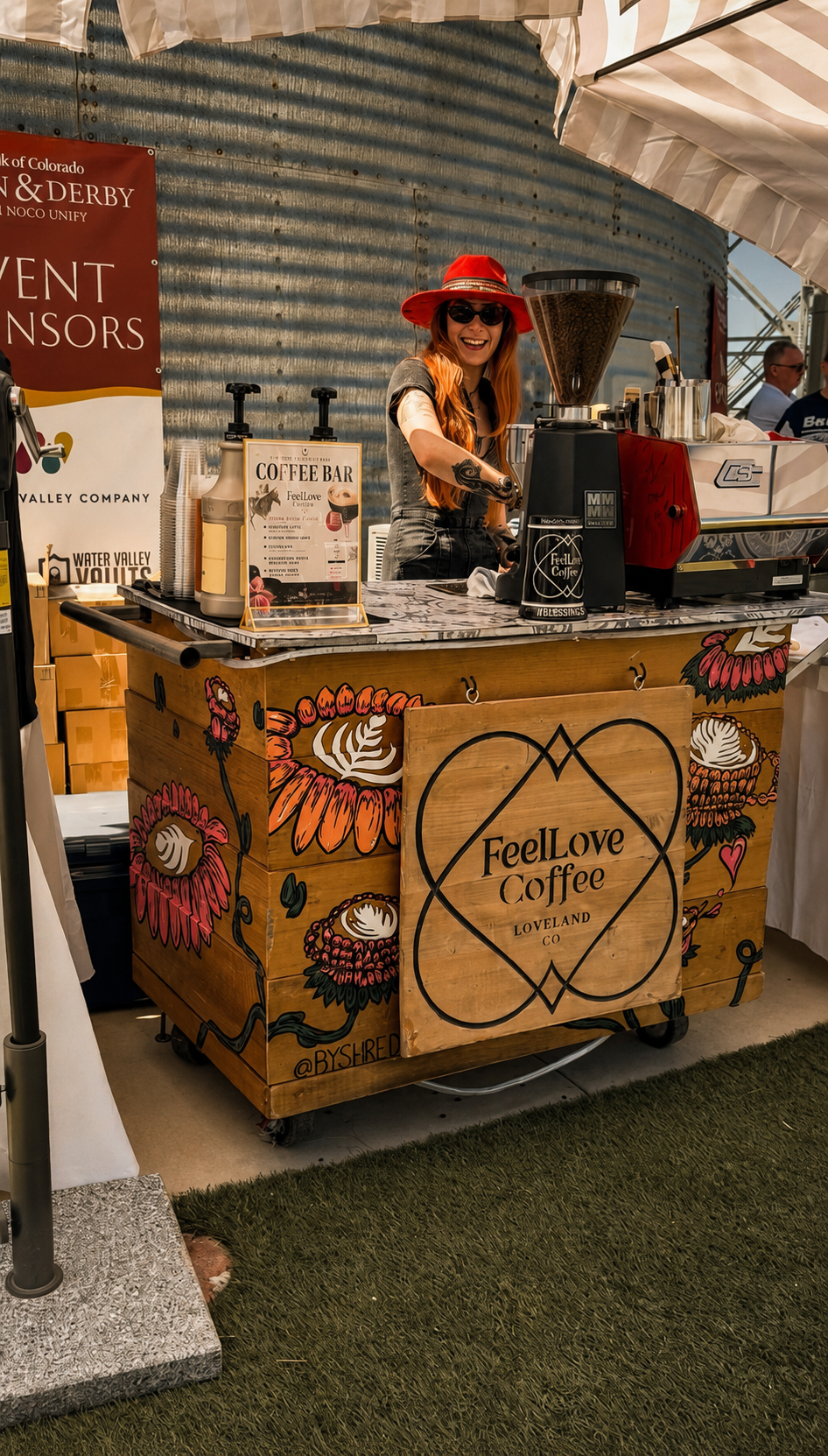 FeelLove Coffee barista in a red hat crafting specialty espresso behind the cart at an outdoor event.